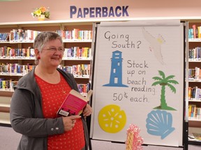 Margaret Christenson, outgoing CEO of the Prince Township Public Library, plans to continue pitching in at library fund-raisers, such as this sale of paperback novels to summer vacationers.