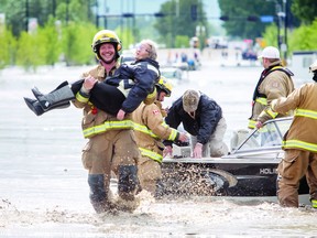 A rescued woman is carried away by a firefighter out of a flood zone in High River on Thursday, June 20, after extreme flooding led to a town-wide evacuation. The flood stretched across southern Alberta, with local RCMP being sent to Calgary to help in relief efforts. Lyle Aspinall/QMI Agency