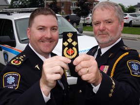 Departing Hastings-Quinte EMS Chief Doug Socha, left, and Acting Chief John O'Donnell hold the latter's new rank epaulet after a county council meeting Thursday in Belleville. Socha is taking a temporary national defence job, with O'Donnell, one of his two deputies, taking his place.