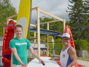 Dan Graham, left, owner of The Cabana Beach House, and James Carrick, surf instructor and paddleboard instructor with the business, hold up a paddleboard at the business on Saturday. Graham said the summer had started slow at the beach, but expects a good season ahead. (Rob Gowan The Sun Times)