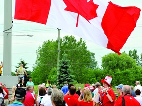 A crowd decked in red and white looks on as a 20 by 40-foot flag is unfurled at Brockville's SmartCentre shopping plaza on Canada Day. (NICK GARDINER/The Recorder and Times)