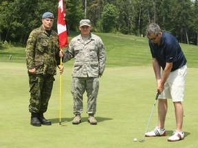 Major Don Saunders lines up a putt on the 18th green
of Osprey Links Golf Course as part of Patriot Golf Day across the country. Canadian and U.S. Troops worked the 18th hole flag sticks at four area courses as part of the event. At left is Private John Stead of Canadian Forces, and holding the flag is Technical Sgt. Jesse Elting, of the U.S Air Force.