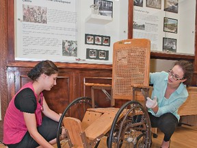 Curatorial assistant Kendra Gerber (left) and curator Chelsea Carss install an early 20th century wheelchair made of wood and wicker, part of a new exhibit at the Brant Museum and Archives in downtown Brantford, Ontario.  The exhibit chronicles the 100-year history of the Brantwood Residential Development Centre, which opened its doors as the Brant Sanatorium in 1913, a residence for tuberculosis patients. (BRIAN THOMPSON Brantford Expositor)
