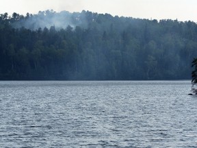 The smoke from the fire rises from the trees along the southern side of Rabbit Lake as people continue to enjoy the water.