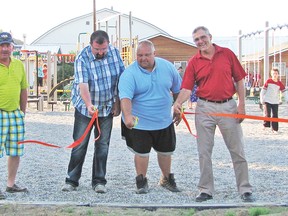 Attending the ribbon cutting at Lomond's new park on July 1 were, from left, Lomond Lions club member Todd Hendricks, Little Bow MLA Ian Donovan, Mayor Brad Koch and Lomond Recreation Board member Ron Schlaht. In the background, some children can be seen already enjoying their new playground. Submitted photo