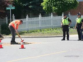 Municipality of Kincardine worker Chris Hartwick fills a hole at the intersection of Broadway of Huron Terrace caused by a broken watermain while South Bruce OPP officers look on. (AMANDA BURLEY/SUBMITTED)