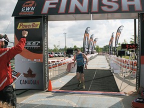 With race director Michael Brown (left) cheering him on, Jeff Symonds hits the tape at the Great White North triathlon in record time, unofficially breaking the previous mark by about three minutes. - Gord Montgomery, Reporter/Examiner