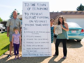 Resident Wendy Henson, far right, and her neighbours Dave and Maria Kratchmer have put signs in front of their homes because they believe the town is responsible for their flood experiences. Henson is holding a copy of the Edmonton Sun which reports on a flood that hit her home in 1996.