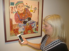 Laura Woermke, St. Thomas Elgin Public Art Centre executive director, uses her smartphone to listen to music picked by staff to accompany artist Kerry Ferris's picture, Old Man and Dog Whip, Grise Fiord. The tune is Rye Whiskey by the Punch Brothers. (Eric Bunnell, Times-Journal)