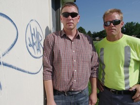 Chris Kern, left, and Graham Reeves of the Woodstock parks deparment stand next to a new batch of grafitti covering the freshly painted rink building in Hunting Estates Park. HEATHER RIVERS/WOODSTOCK SENTINEL