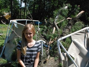 Pyper Averhoff, 10, sits on the pine that crushed her pool after a micro burst of wind tore through the middle of Callander Friday morning. Neighbours and friends were helping each other clean up and assess the damage Saturday.