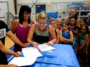 Dominique Pegg, centre, signs a letter of intent to the University of Alabama while her mom, Cathi Parker, third from left, coaches Liz and Dave Brubaker and her teammates at Bluewater Gymnastics look on Monday, July 22, 2013 at Bluewater Gymnastics in Sarnia, Ont. PAUL OWEN/THE OBSERVER/QMI AGENCY