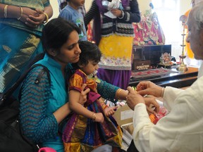 Sushil Kalia, a Hindu priest from Edmonton, ties Kalava—sacred Hindu red thread—on the wrists of Sailaja Pammidi and her 20-month-old daughter, Tejaswi Pammidi at the official opening of the first Hindu temple in Grande Prairie on Sunday. The new cultural centre marks the northernmost Hindu temple in Canada. (Caryn Ceolin/Daily Herald-Tribune)