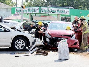 Chatham-Kent firefighters tend to a Chatham woman behind the wheel of a red Hyundai Accent until paramedics arrived at the two-vehicle crash on Queen Street at Park Avenue West in Chatham, Ontario at about 10 a.m. on Wednesday July 31, 2013. The woman was taken by ambulance to hospital where she was treated for minor injuries. A Blenheim man driving the white Chrysler told police he was southbound when the northbound Hyundai turned in front of him. (VICKI GOUGH, The Daily News)