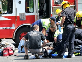 The driver of a motorcycle is tended to by paramedics and firefighters following a crash involving a Fed Ex truck on St. Clair Street Thursday afternoon. Police said charges are pending against the driver of the truck. The motorcyclist was transported to hospital with injuries to his leg. (Diana Martin, Chatham Daily News)