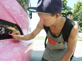 Shawn Loken watches as Jason Peters adds his name to thousands of permanent signatures on the Canadian Breast Cancer Foundation's pink bus when the Pink Tour visited North Bay on Friday to promote disease prevention and awareness. (MARIA CALABRESE The Nugget)