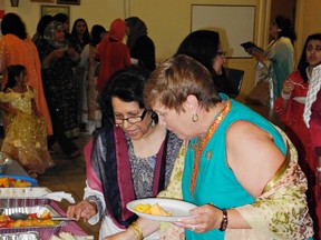 Khalida Uddin (left) encourages Karen Williamson to sample some of the savoury treats that were part of celebrations held at the end of a month of fasting during Ramadan. (Expositor photo)