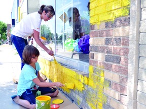 Madeline Lee, seated, and her mother Colette, paint the outside of iDecor and More, in downtown Portage la Prairie, a cheery "sunflower" yellow. Colette and her husband Eric are co-owners of the home improvement retailer. (CLARISE KLASSEN/PORTAGE DAILY GRAPHIC/QMI AGENCY)
