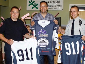 Blake Richards, centre, and fire dept. Lt. Marlin Glaspey, left, and Cst. Kyle MacDonald pose with their jerseys for the upcoming charity hockey game.