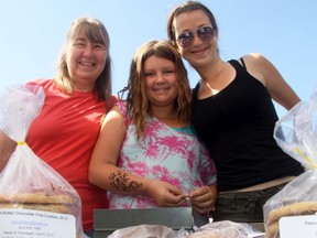 Pam Luscombe, daughter Ashley, and granddaughter Kylee pose at the Cochrane Farmers Market where they sell all their baked goods every week.  Ashley helps bake and Kylee sells while daughter Megan handles the marketing and husband Bob Luscombe helps set up and tear down each week at the Farmer's Market.