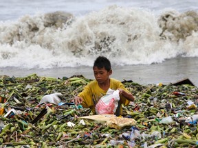 A boy sifts through floating garbage as he collects recyclable items to sell while strong waves crash along the shores of Manila Bay, near a slum area in Manila August 12, 2013. REUTERS/Romeo Ranoco