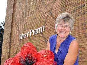 Annamarie Murray, West Perth Coun. and member of the West Perth Tourism & Community Beautification Committee, ties a bow onto the railing outside the municipal building on St. David Street in Mitchell. The committee is selling the red and black bows to help raise money for committee beautification projects and to show community support for the IPM later this month.