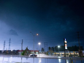 A flash of lightning lights up the sky as a car drives through a large puddle in London, Ont., on Wednesday. (DEREK RUTTAN/QMI Agency)