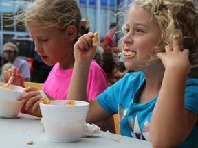 Charlize Wildschut, 7, left, and her sister Ariah, 6, enjoy a hearty dinner at the One Tomato Souper Day Thursday. Volunteers handed out free locally produced soup outside the downtown Sarnia library branch thanks to a grant from the Awesome Foundation Sarnia. BARBARA SIMPSON / THE OBSERVER / QMI AGENCY