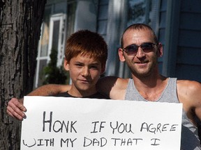 Brian Holcolmbe, left, holds up a sign on Murray Street, as his dad Casey Holcolmbe looks on, on Sept. 26. Casey Holcolmbe made his son hold up the sign after he received a call about his son's behaviour at school on three consecutive days.