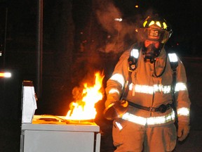 Firefighter Cody Feltz demonstrates the proper way to extinguish a grease fire on an overheated stove by covering it. Never throw water on an overheated pan of cooking oil, just cover it, turn off the burner and let it cool on its own. ANDY BADER/MITCHELL ADVOCATE