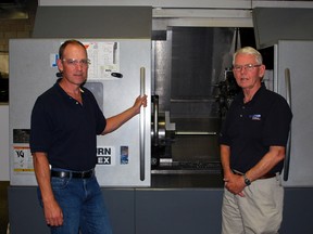 Owners Ian, left, and Jack Wagter of Lumar Machining and Manufacturing stand next to a computer numeric control (CNC) machine in their Burwell Rd. plant on Tuesday. The automated machines are helping drive Lumar's expansion because they can do multiple complex operations and repeat them with high consistency and speed.