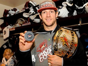 Verona’s Mike Smith of the Phoenix Coyotes holds the puck from his first NHL goal against the Detroit Red Wings, as well as the team’s player-of-the-game belt, while his son Aksel, 3, sits at Smith’s dressing room stall at Jobing.com Arena on Saturday in Glendale, Ariz. Smith scored with one-tenth of a second left in the game in the Coyotes’ 5-2 win. (Norm Hall Photography)