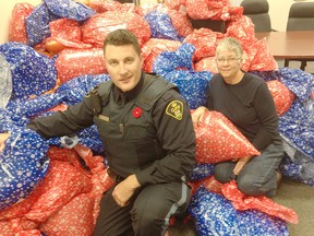 Prince Edward OPP Const. Anthony Mann and Adopt-A-Child volunteer Barb Sills are pictured with the mountain of gift bags filled with winter clothing given out on the weekend. With donations dwindling, the Adopt-A-Child program is facing financial difficulties.