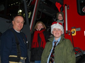 St. Thomas firefighter Warren Scott, stands with Ally, Isaiah and Nathaniel Kuhn in the main fire hall on Saturday. The siblings got to ride in a fire truck during Saturday's Optimist Club of St. Thomas Santa Claus Parade because they help run an annual campaign that recognizes area emergency workers.