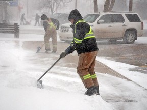 Town crewmen Jeff Woods, foreground, and Kent Broere begin the battle against the elements Monday morning, clearing snow off sidewalks. There is currently an advisory on poor winter driving conditions on major highways.
