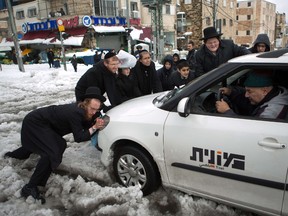 Ultra-Orthodox Jews push a car stuck in the snow on a road in Jerusalem on December 13, 2013 following a snowstorm. The hilltop city of Jerusalem was paralysed today by its fiercest snowstorm in years, with its mayor calling out the army to help stranded motorists. Main roads into the Holy City, which climb around 795 metres (2,600 feet) above sea level were closed and police appealed to drivers not to attempt the journey. AFP PHOTO/MENAHEM KAHANA