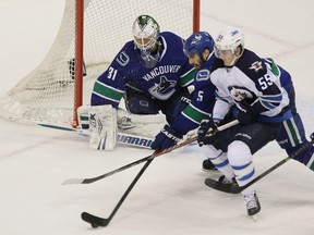 Winnipeg Jets ' Mark Scheifele (right) applies pressure to Vancouver Canucks’ Jason Garrison (centre) as he steers the puck away from Vancouver Canucks’ goalie Eddie Lack (left) during the second period of NHL hockey at Rogers Arena in Vancouver, B.C. on Sunday December 22, 2013. Carmine Marinelli/Vancouver 24hours/QMI Agency