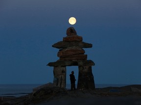 A man looks at a giant inukshuk as the moon rises above it in Rankin Inlet, Nunavut August 21, 2013.  REUTERS/Chris Wattie