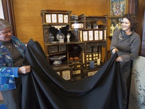 Eldon House staff members Barb Fieldhouse, left, and Tara Wittmann, unveil a carefully restored 19th-century Japanese cabinet at the downtown museum in London on Sunday. The piece is back on display after an 18-month restoration. (CRAIG GLOVER, The London Free Press)