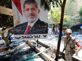 A member of the military police stands beside a poster of deposed Egyptian President Mohamed Mursi that reads: "No to the coup - The president of all Egyptians" amid the debris of a cleared protest camp outside the burnt Rabaa Adawiya mosque in Cairo on Aug. 15, 2013. 
REUTERS/QMI Agency