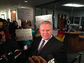 Councillor Doug Ford speaks to reporters on Tuesday in front of Mayor Rob Ford's office while protesters look on. (DON PEAT/Toronto Sun)