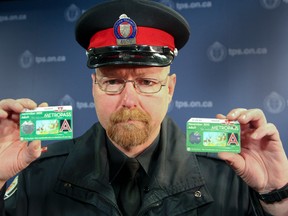 Const. Bob Moynagh holds a counterfeit Metropass in his left hand and the real one in the right at Toronto Police headquarters Wednesday, February 12, 2014. (Veronica Henri/Toronto Sun)