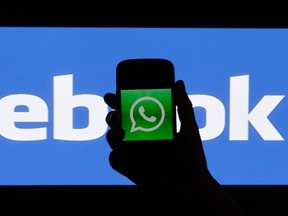 A woman holds a smartphone displaying WhatsApp's logo in front of the screen with the Facebook logo in this photo illustration. Facebook purchased WhatsApp for $19 billion. (REUTERS/David W Cerny)