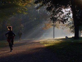 A woman runner is lit by early morning sun and mist as she runs through Springbank Park. Photo by Mark Spowart.