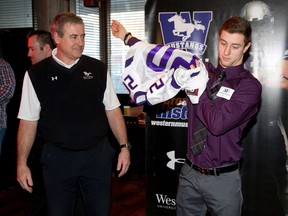 Western Mustangs football head coach Greg Marshall watches as recruit Mackenzie Ferguson of London puts on a Mustangs jersey at Lone Star Texas Grill Thursday. Ferguson, a SPECTRA winner from Banting, did everything for the Broncos last year but the Mustangs will use him as a defensive back. (CRAIG GLOVER, The London Free Press)