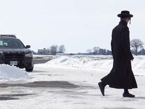 A member of the ultra-orthodox Lev Tahor sect walks across the roadway leading into their enclave at Spurgeon's Villa, north of Chatham, Ont., while Chatham-Kent police keep watch over the community on Wednesday, March 5, 2014. (VICKI GOUGH/ QMI AGENCY)