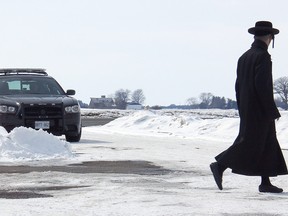 A member of the ultra-orthodox Lev Tahor sect walks across the roadway leading into their enclave at Spurgeon's Villa, north of Chatham, Ont., while Chatham-Kent police keep watch over the community on Wednesday, March 5, 2014. VICKI GOUGH/ THE CHATHAM DAILY NEWS/ QMI AGENCY
