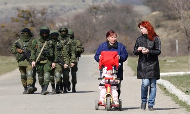 Women talk as they take a walk with a child in a pram while armed men, believed to be Russian servicemen, follow them outside a Ukrainian military base in Perevalnoye, near the Crimean city of Simferopol, March 14, 2014. A Russian warship unloaded trucks, troops and at least one armoured personnel carrier at a bay near Sevastopol in Crimea on Friday morning, as Moscow continued to build up its forces on the Ukrainian peninsula.  REUTERS/Vasily Fedosenko (UKRAINE - Tags: POLITICS MILITARY TPX IMAGES OF THE DAY)