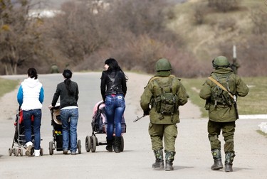 Women with their children in prams walk as armed men, believed to be Russian servicemen, follow them outside an Ukrainian military base in Perevalnoye, near the Crimean city of Simferopol, March 14, 2014. Russia shipped more troops and armour into Crimea on Friday and repeated its threat to invade other parts of Ukraine, showing no sign of listening to Western pleas to back off from the worst confrontation since the Cold War.  REUTERS/Vasily Fedosenko (UKRAINE - Tags: POLITICS MILITARY)