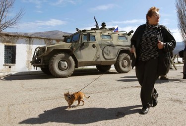 A woman walks her dog past an armed man, believed to be a Russian serviceman, standing guard outside a Ukrainian military base in Perevalnoye, near the Crimean city of Simferopol, March 14, 2014. Russia shipped more troops and armour into Crimea on Friday and repeated its threat to invade other parts of Ukraine, showing no sign of listening to Western pleas to back off from the worst confrontation since the Cold War.  REUTERS/Vasily Fedosenko (UKRAINE - Tags: POLITICS MILITARY ANIMALS)